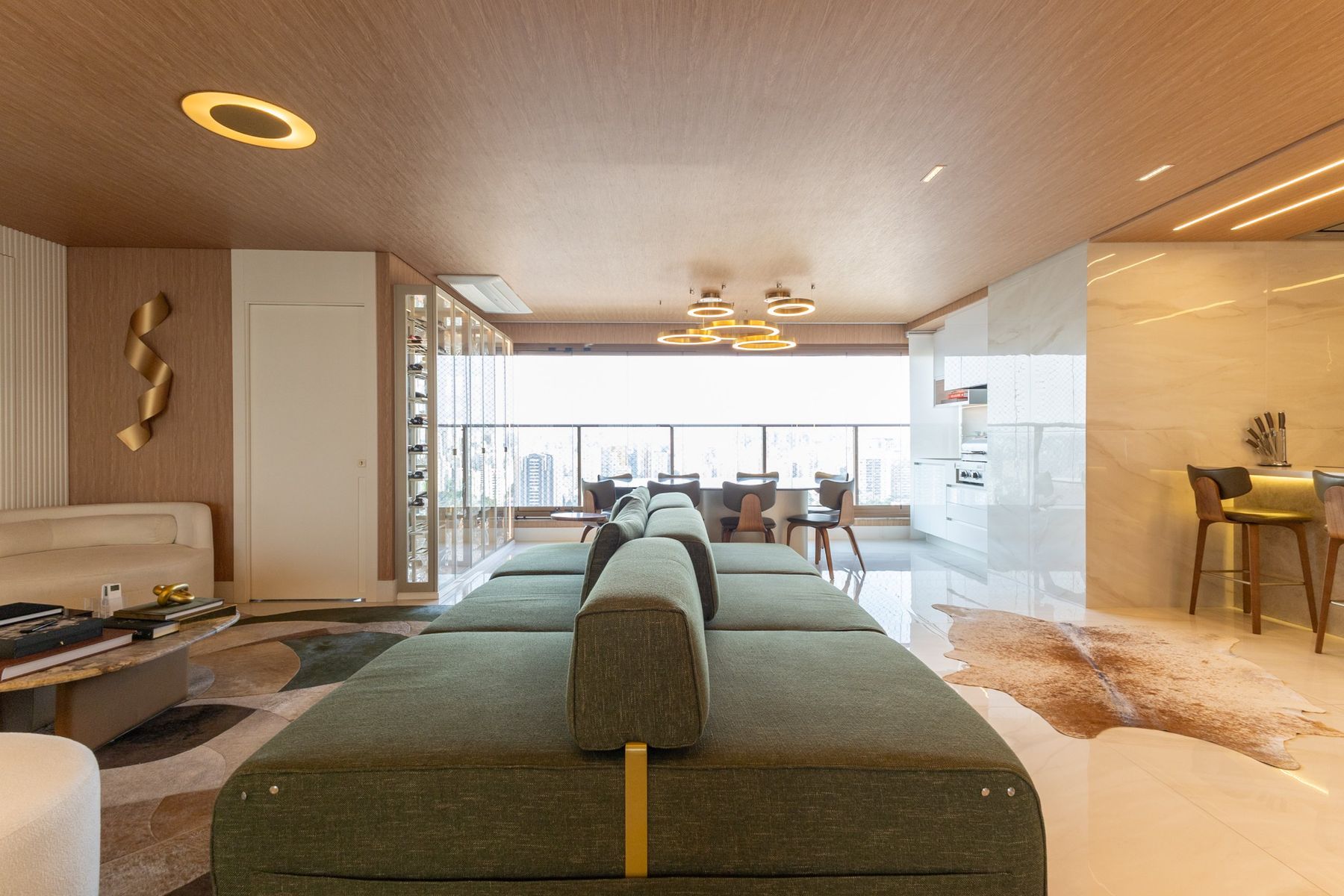 Apartamento em Campo Belo, projeto de 2024: sala integrada com sofá verde, forro em madeira, pendentes dourados e vista da cidade